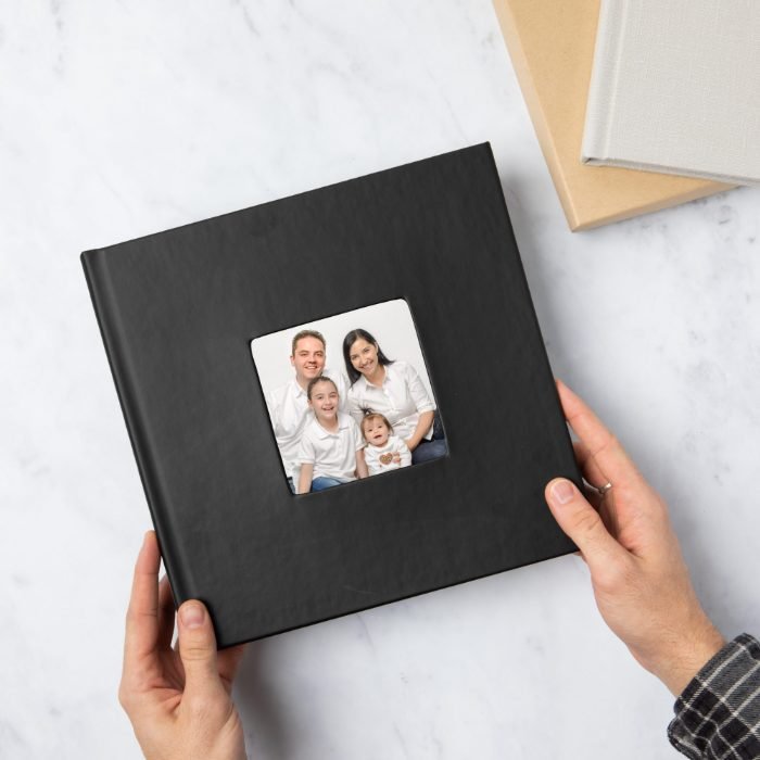 Hands holding a black leather family album with a photo inset set into the cover