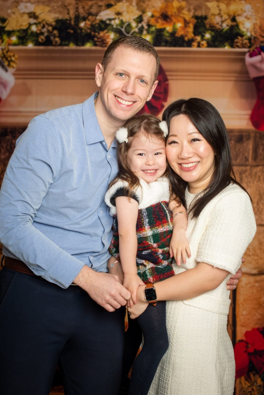 Family of three smiling together by a decorated mantel during a holiday photo session