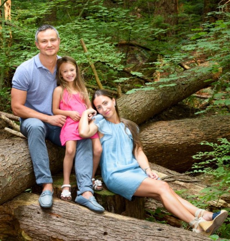 Family of three sitting on fallen logs on a forested trail