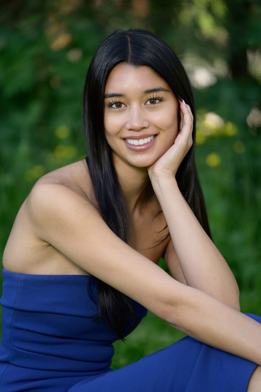 Graduate in a blue dress seated in a wildflower meadow