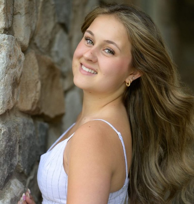 Graduate in a white dress photographed against a stone wall during her grad session in Langley, BC
