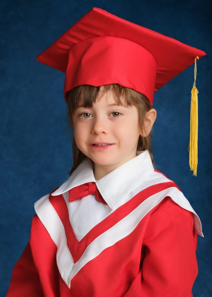 Preschool graduation portrait of a girl in a red cap and gown with a gold tassel