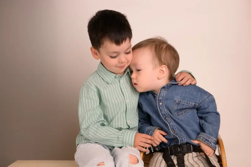 An older brother with his arm around his baby brother in a studio sibling portrait