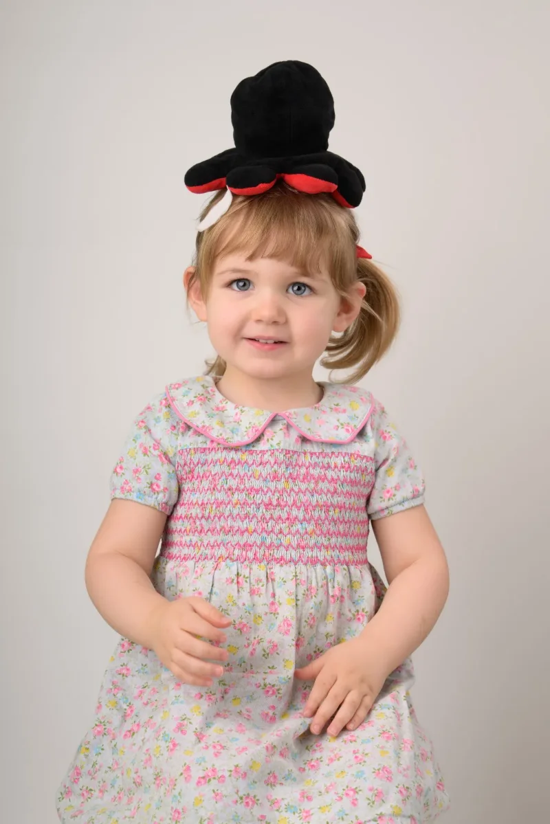 The same toddler balancing a black felt top hat on her head, grinning at the camera