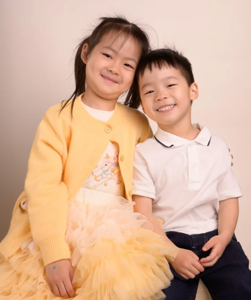 A sister in a yellow cardigan standing beside her little brother