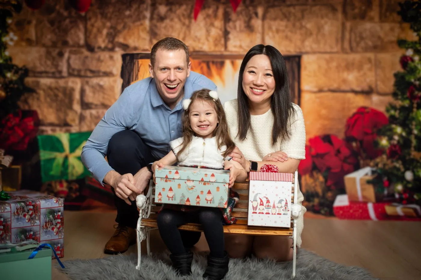 Parents and their toddler with wrapped gifts on the fireplace set during a Christmas mini session