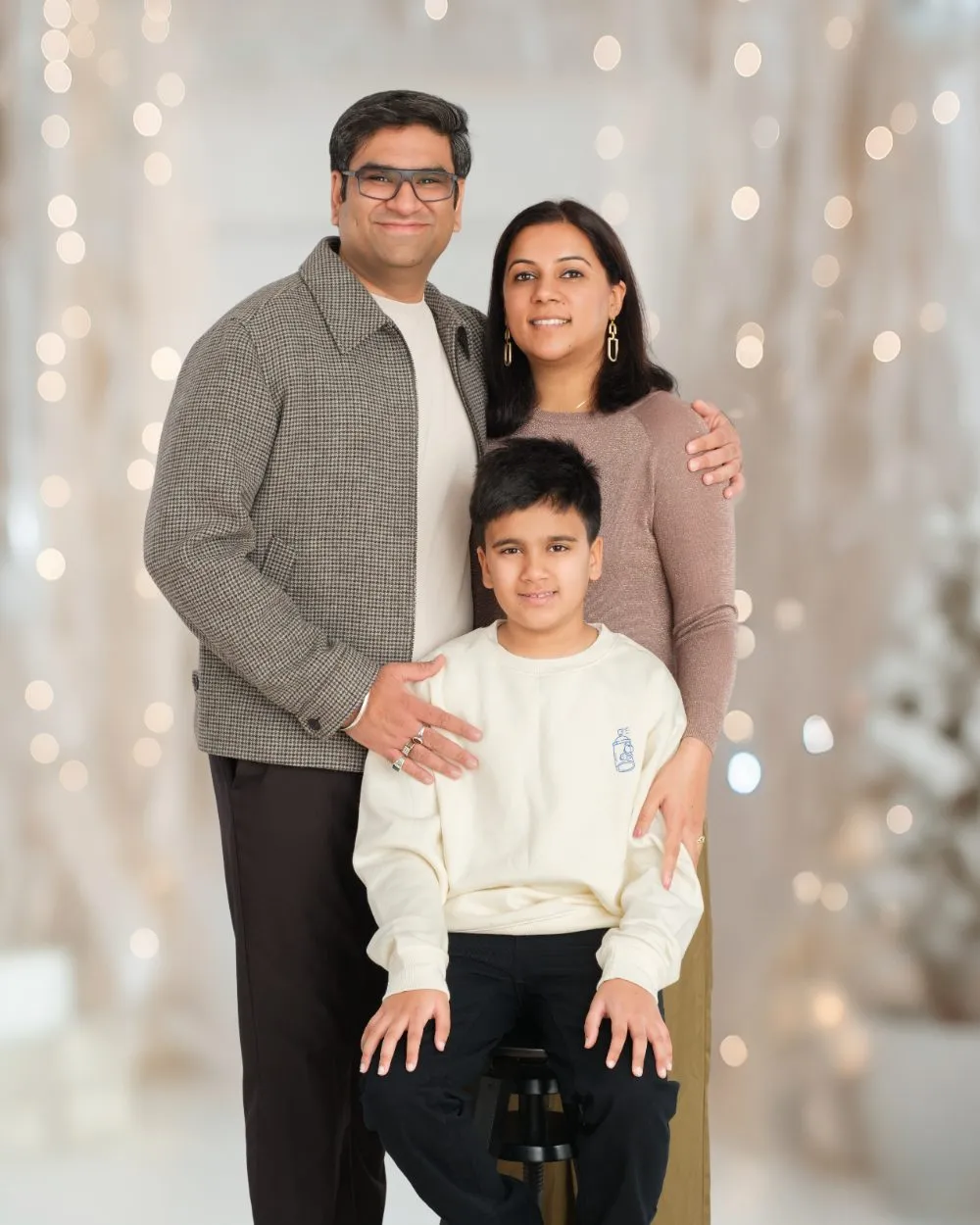 Parents standing with their son on a stool in front of warm holiday lights