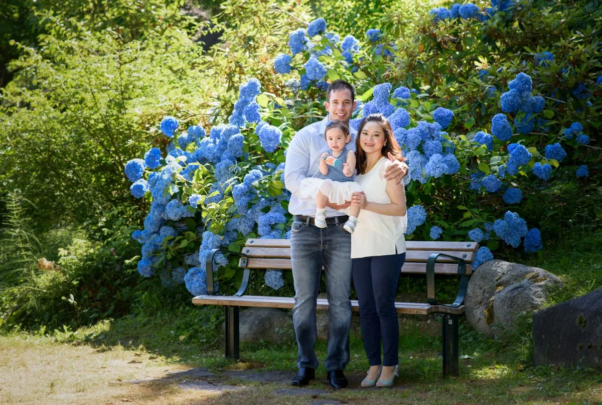 Family standing with their baby daughter in front of blue hydrangeas during an outdoor mini session