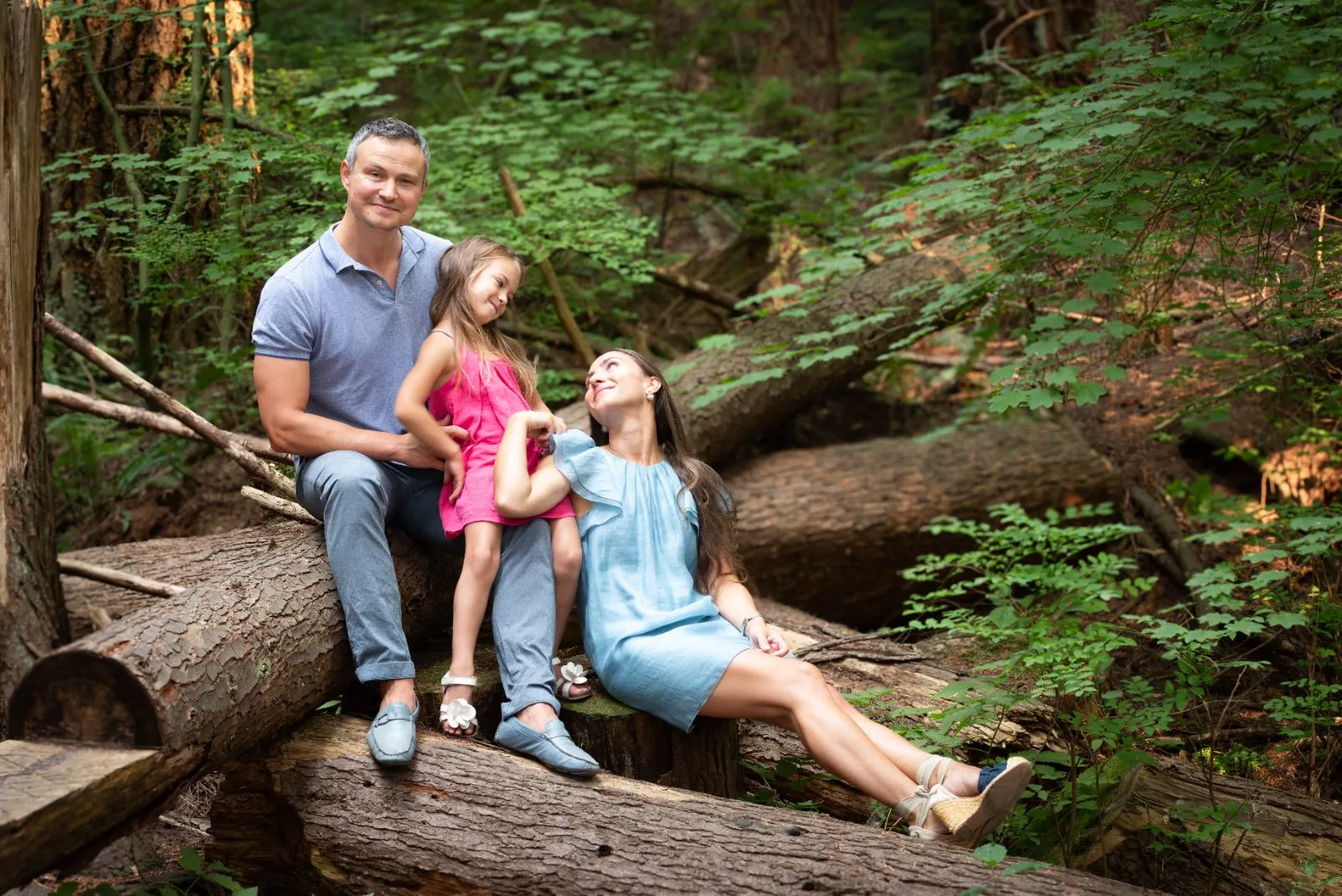 Parents and their young daughter sitting on a fallen log in the forest during an outdoor family mini session near Langley