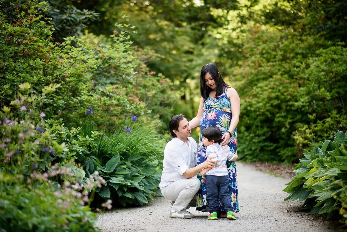 Expecting parents and their toddler son on a garden path during an outdoor maternity session