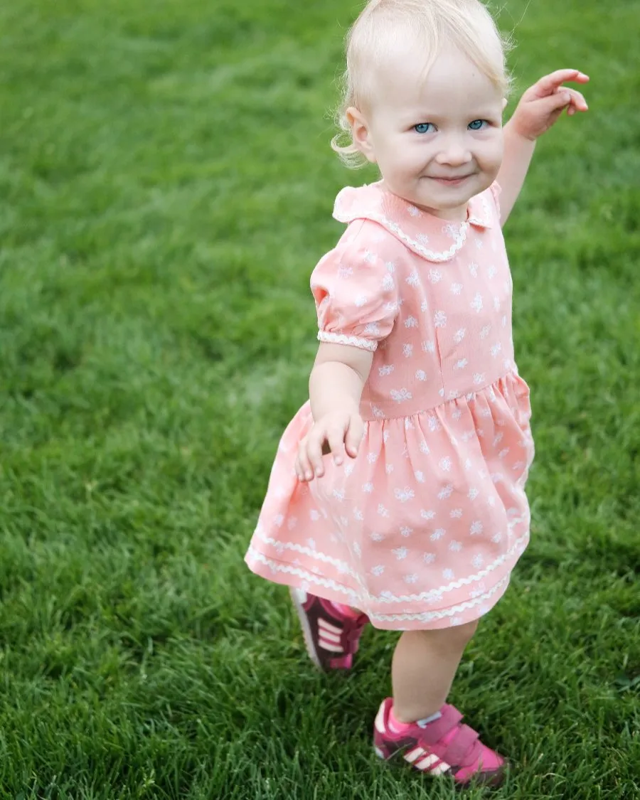 Toddler in a pink dress walking across the grass during an outdoor mini session