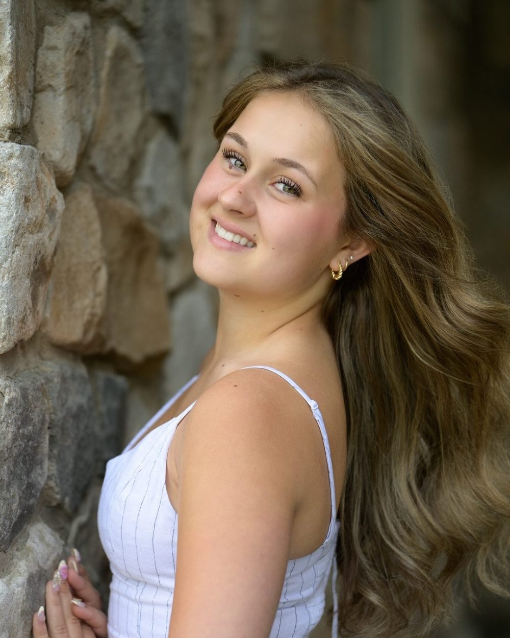 Grad portrait of a smiling young woman leaning against a stone wall outdoors