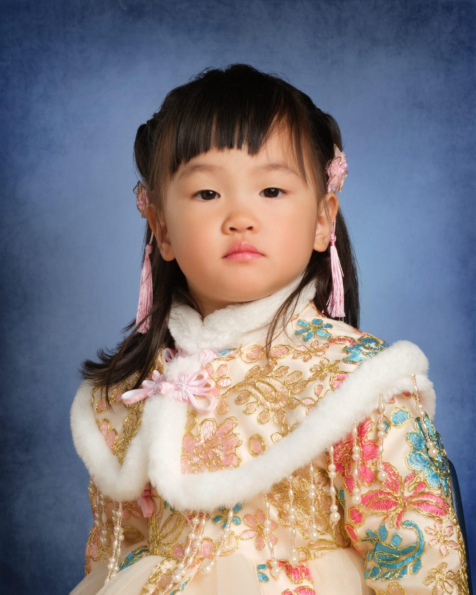 A preschool portrait of a girl in an embroidered outfit on a classic blue school-photo backdrop