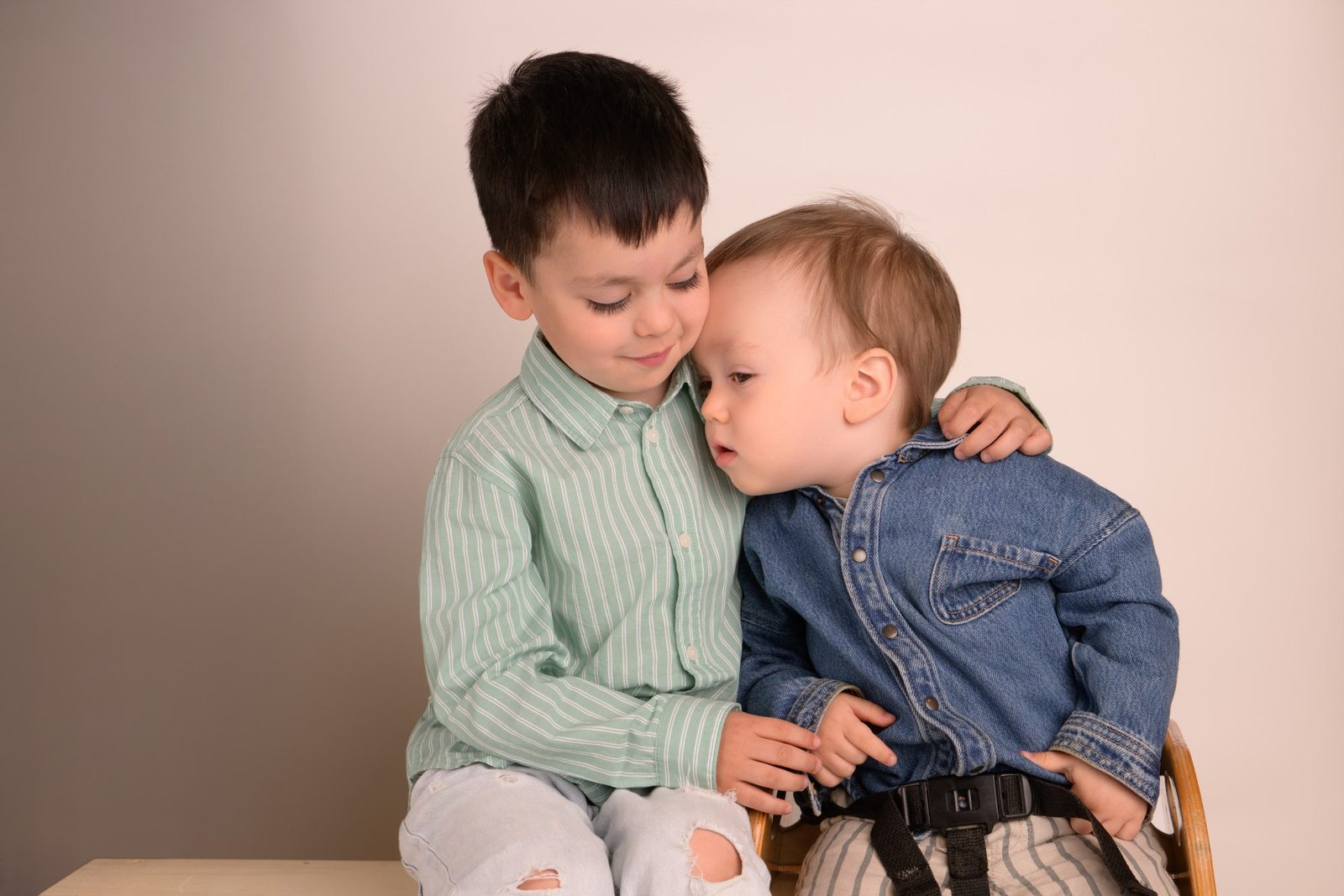 An older brother with his arm around his baby brother in a studio sibling portrait