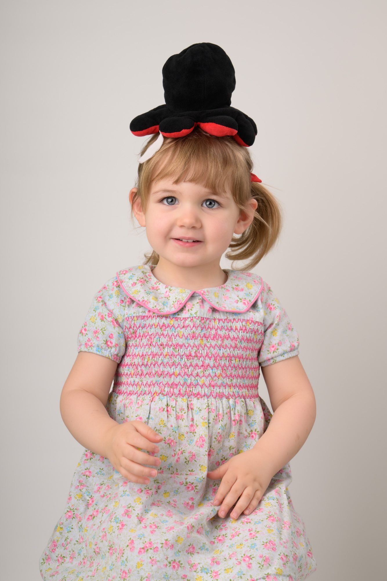 The same toddler balancing a black felt top hat on her head, grinning at the camera