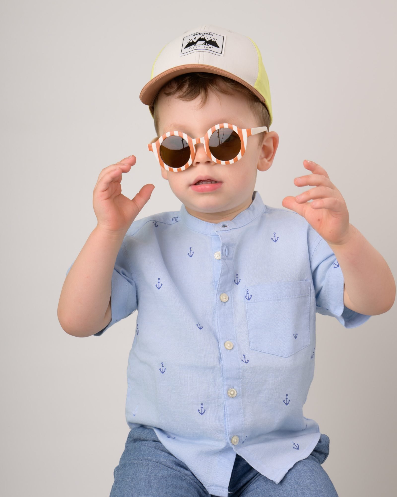 A toddler being silly in a ball cap and round play sunglasses on photo day