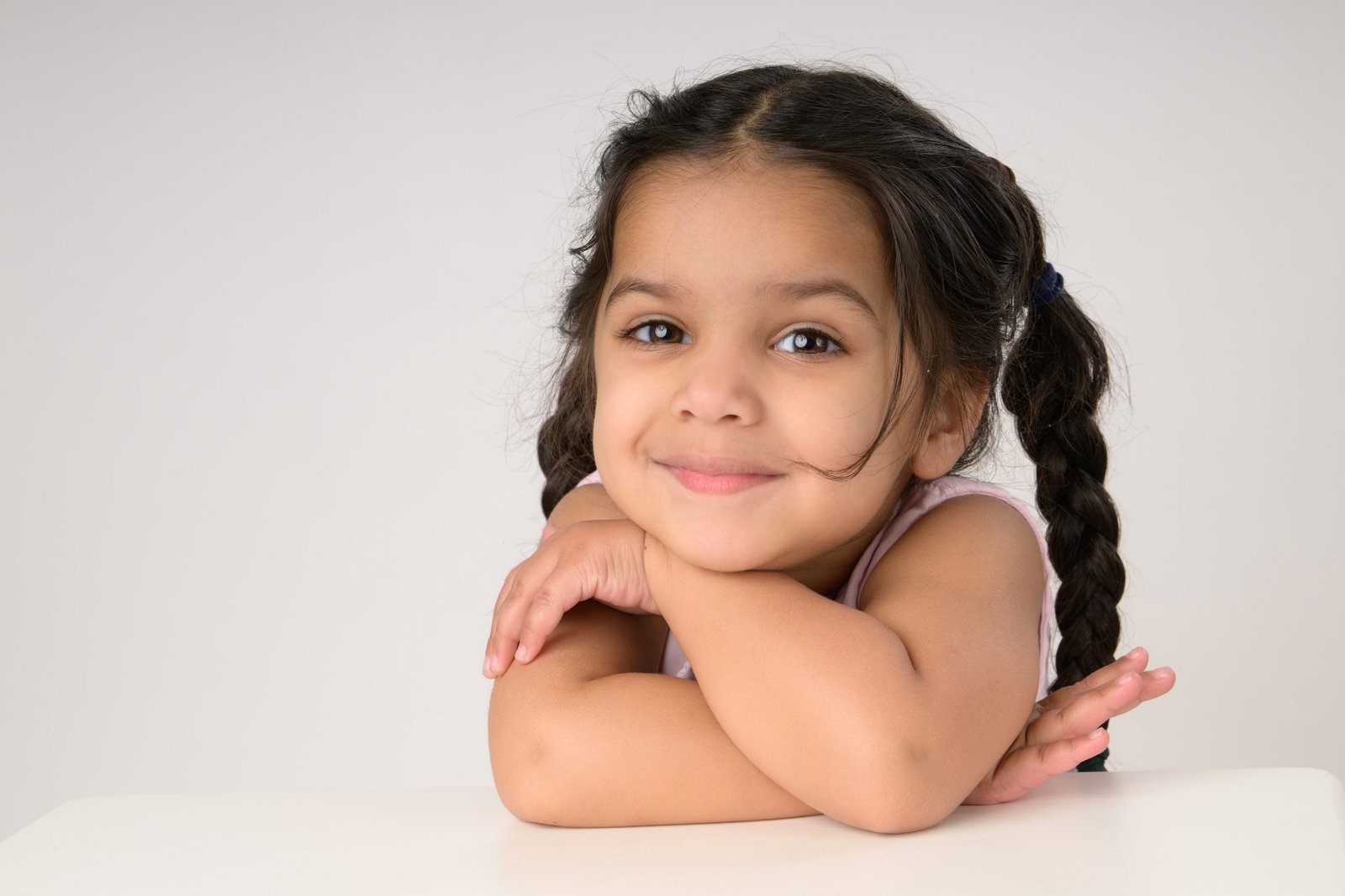 A girl with braids resting her chin on her folded arms, smiling gently