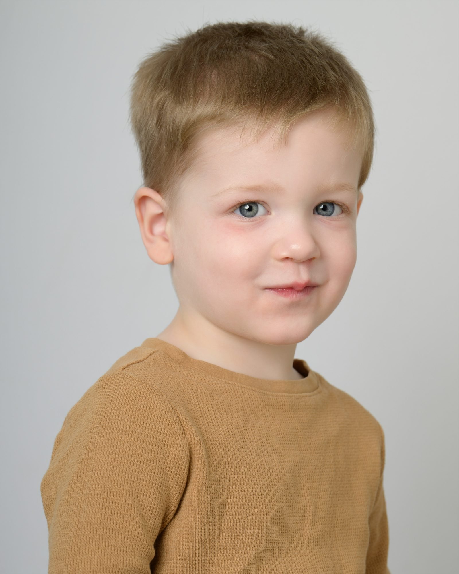 A quiet portrait of a young boy in a tan waffle shirt on a soft grey studio backdrop