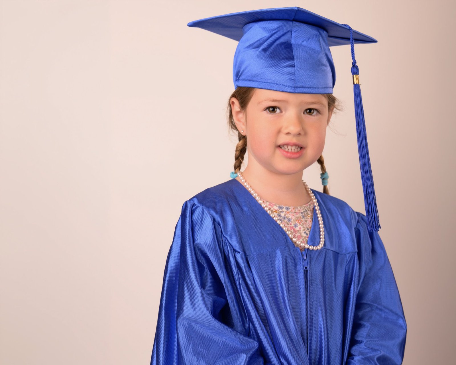 A preschool graduate in a blue cap and gown wearing a pearl necklace