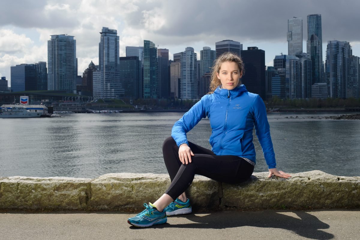 Activewear brand photography of a model seated on the seawall with the Vancouver skyline behind