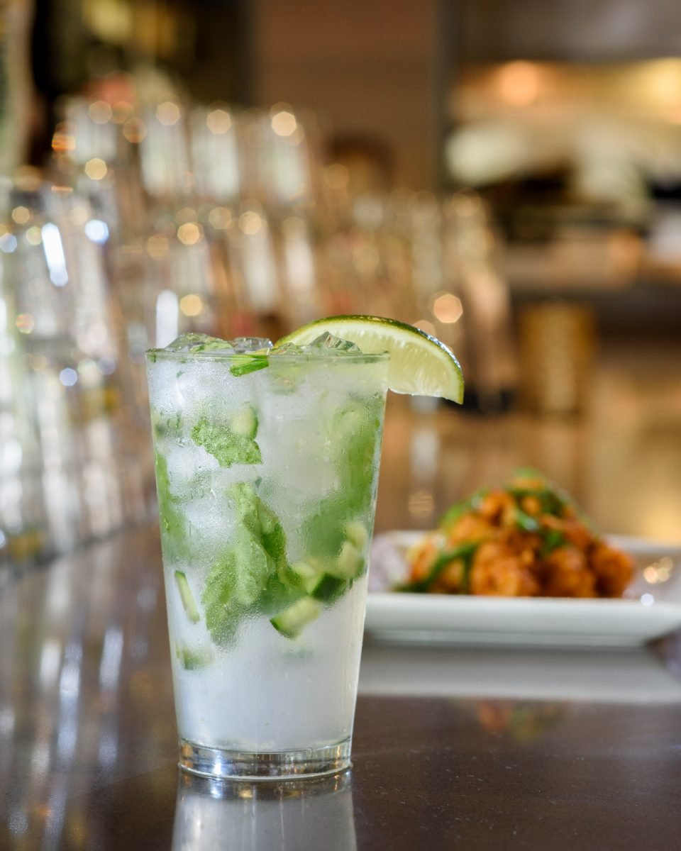 Drink photography of a cucumber and lime cooler on a restaurant bar with cauliflower bites behind