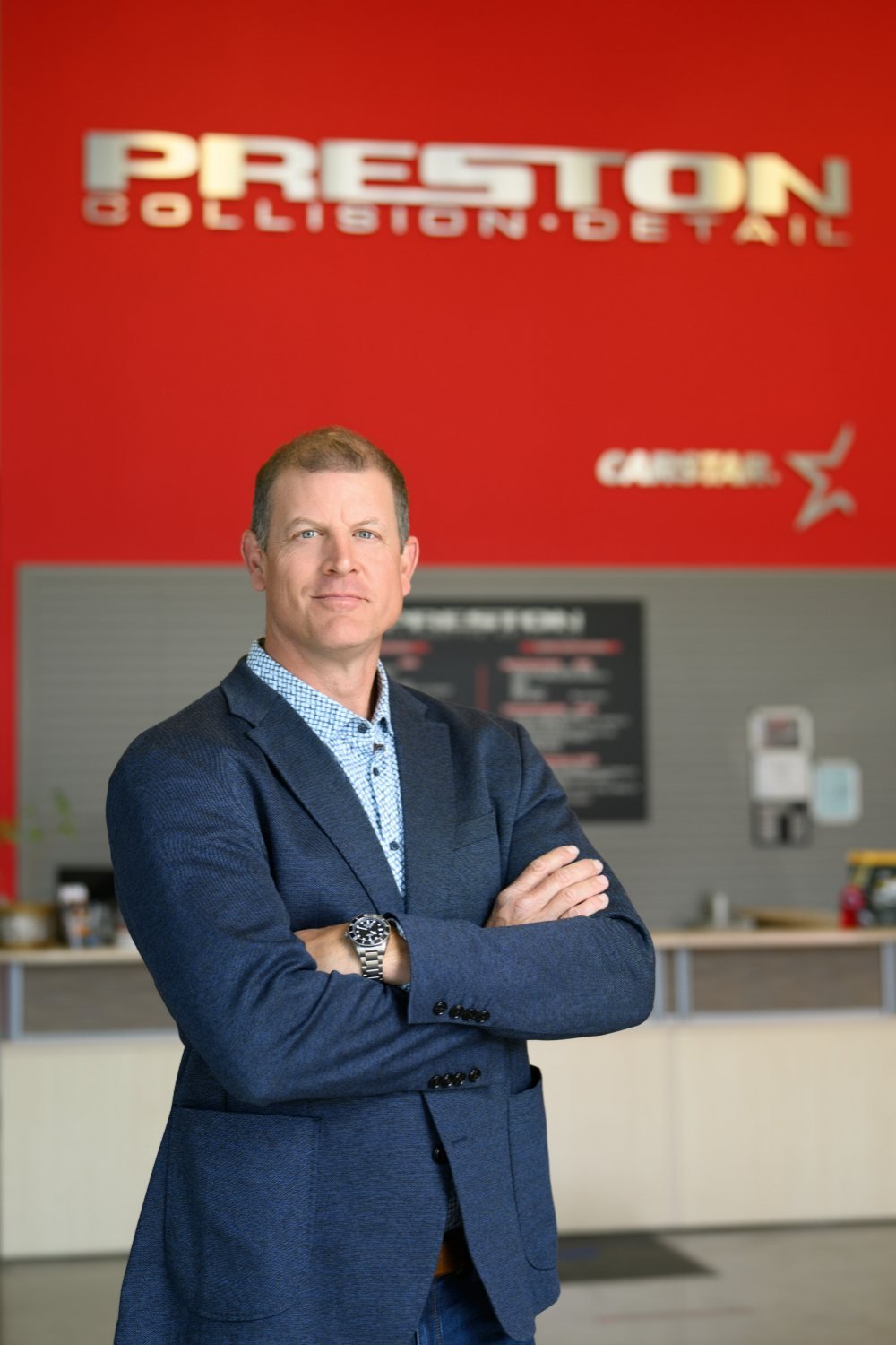 Commercial portrait of a collision repair business owner in front of the red Preston Collision & Detail wall in Langley BC, Volkan Photography