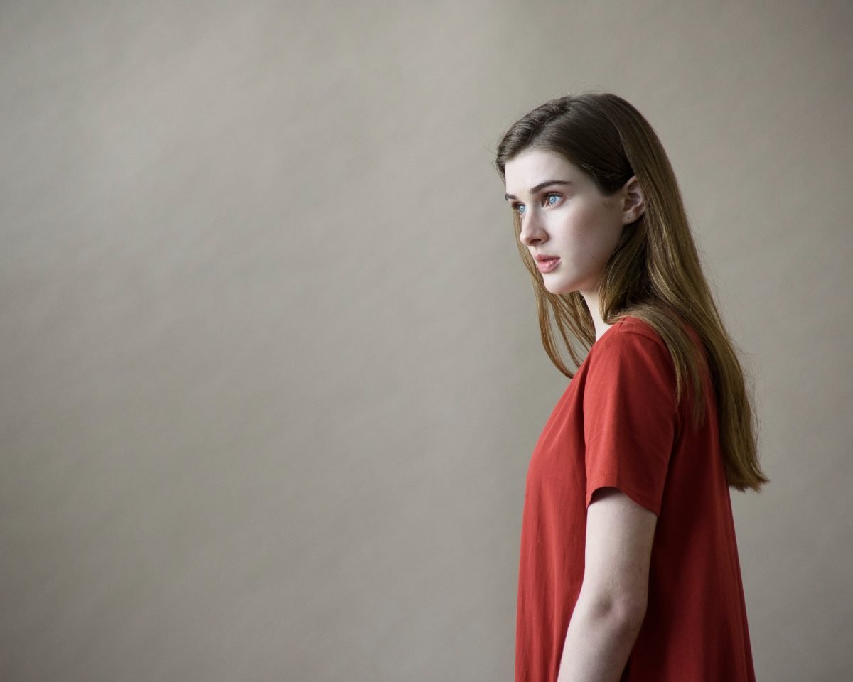 Apparel photography of a model in profile wearing a rust red tee against a soft grey studio wall