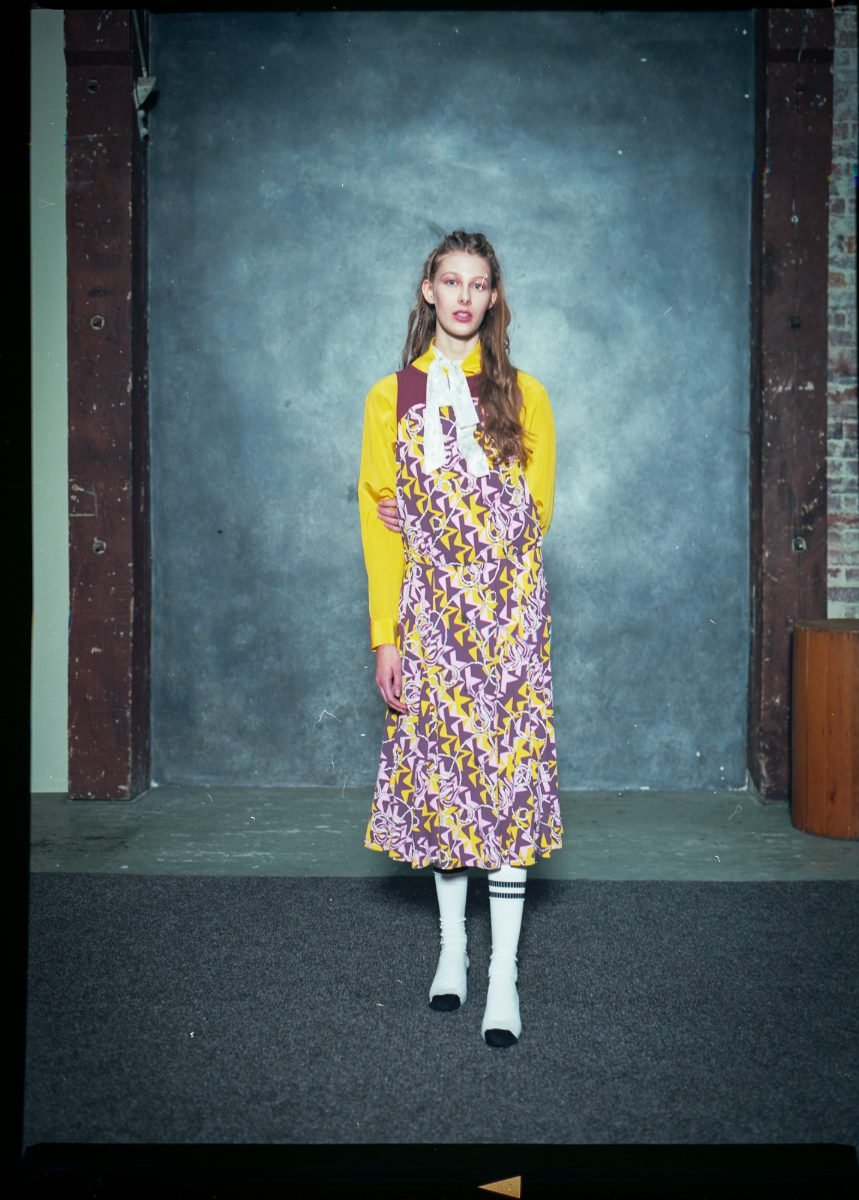 Film fashion editorial photography of a model in a printed pinafore dress on a painted studio backdrop