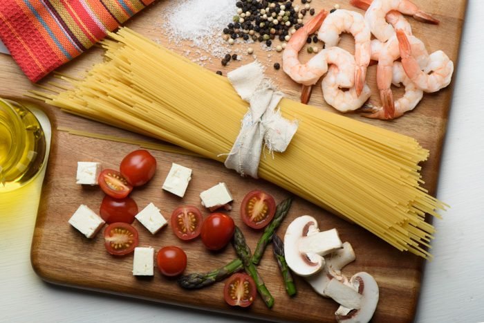 Overhead food photography flat lay of spaghetti, prawns, tomatoes and feta on a wooden board