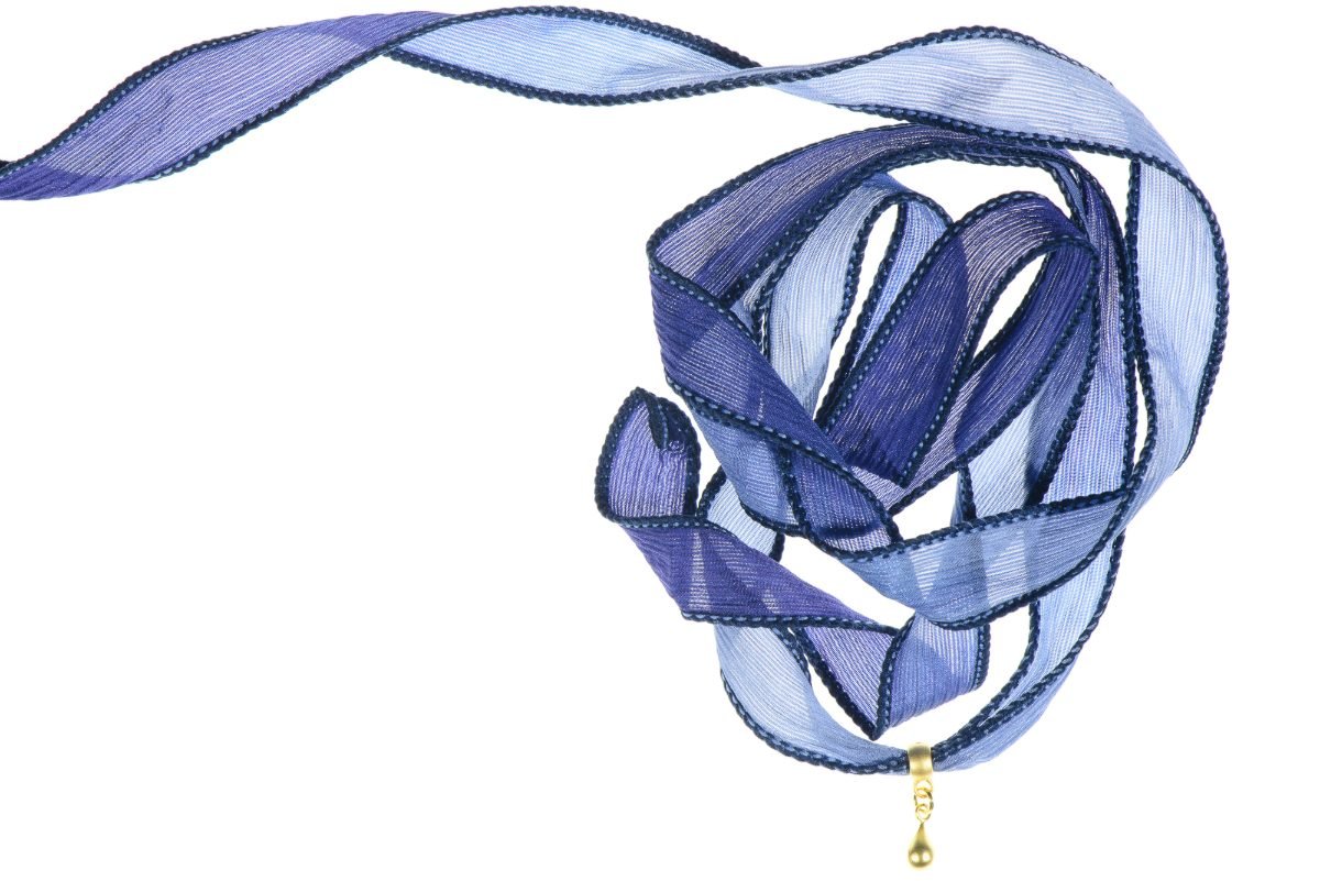 Accessory packshot of a coiled indigo silk ribbon wrap with a gold drop charm on pure white