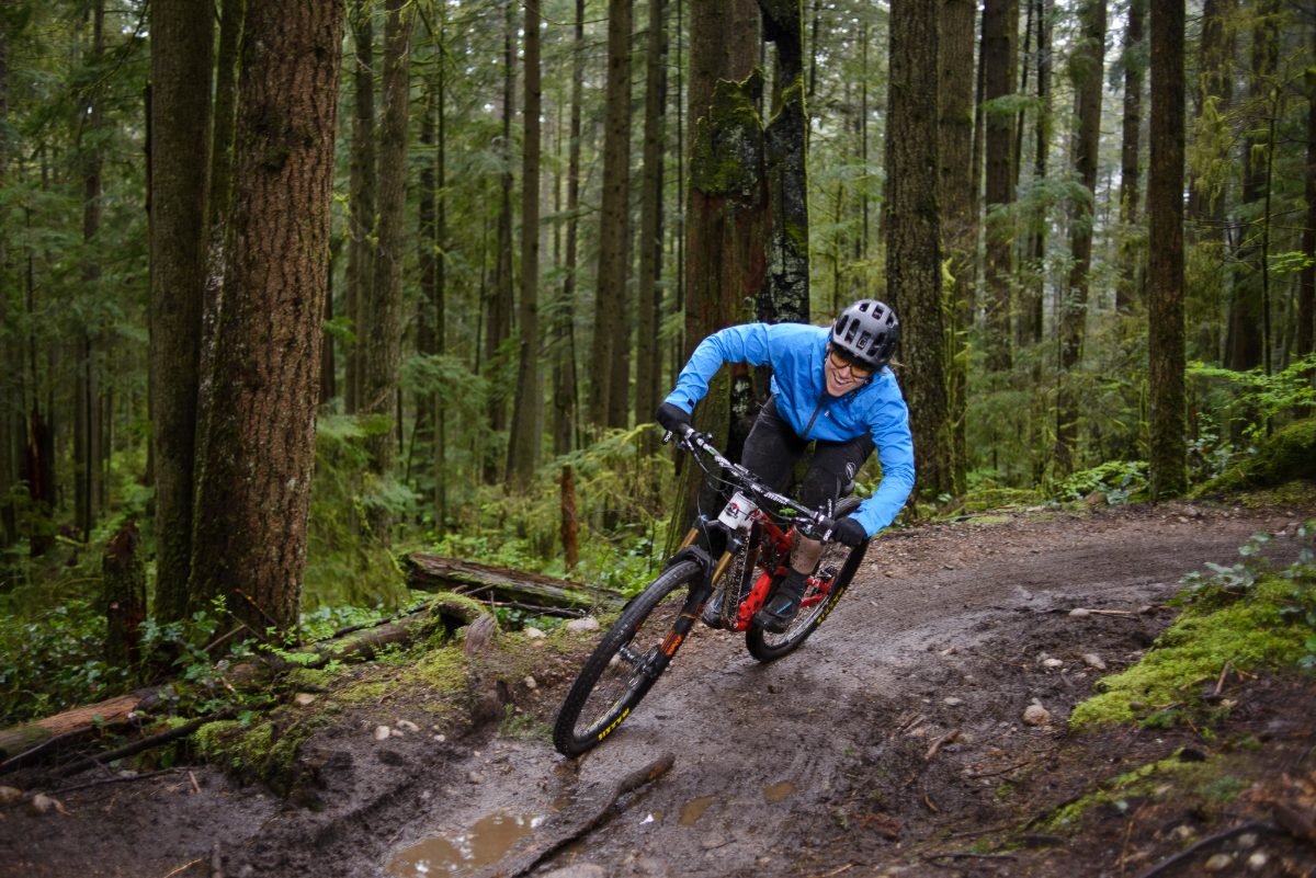Cycling brand photography of a rider mid-jump on a BC single track in the rain forest