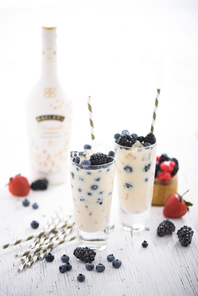 Bright product photography of two iced cream liqueur drinks with blackberries on white painted wood