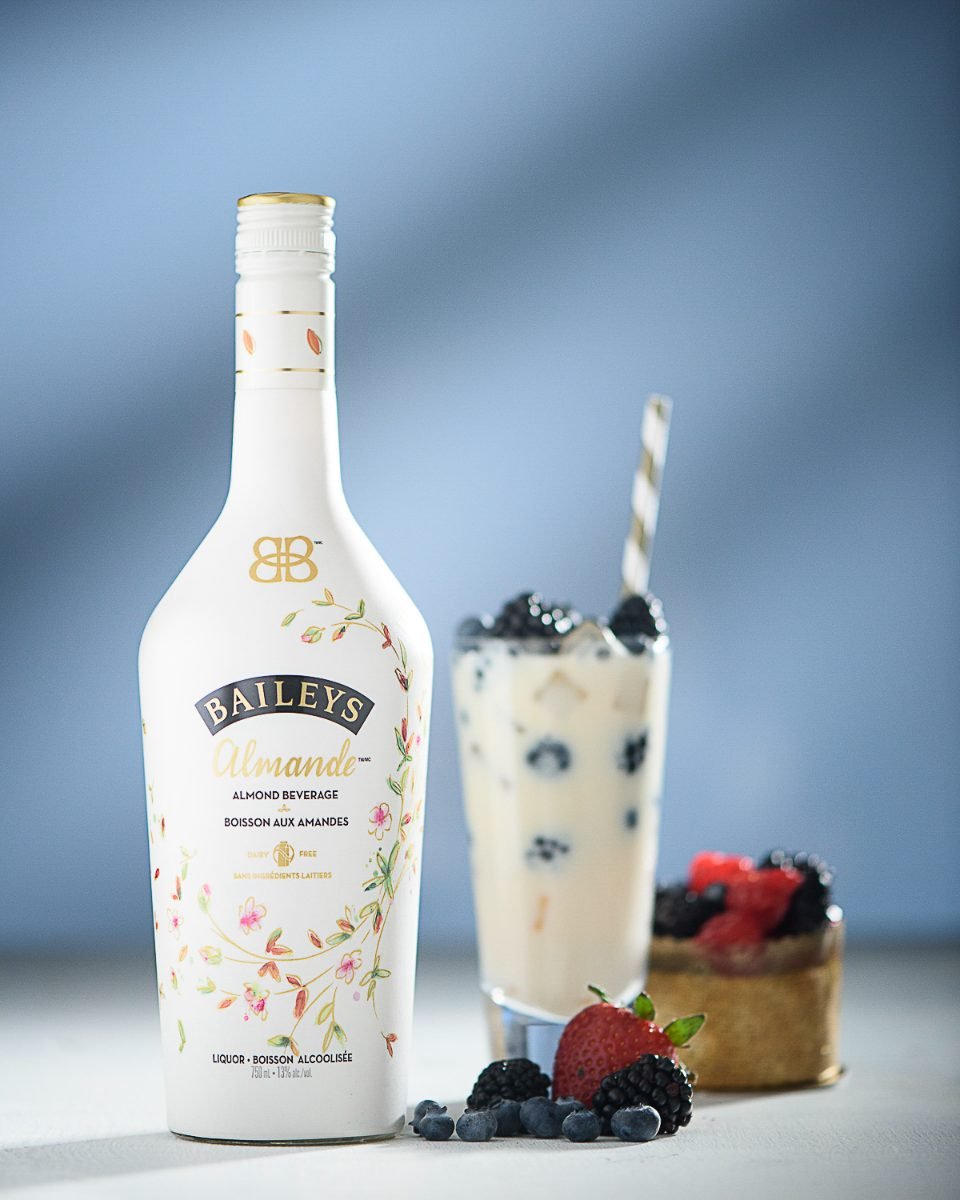 Styled beverage product photography of a cream liqueur bottle with a berry tart and iced glass