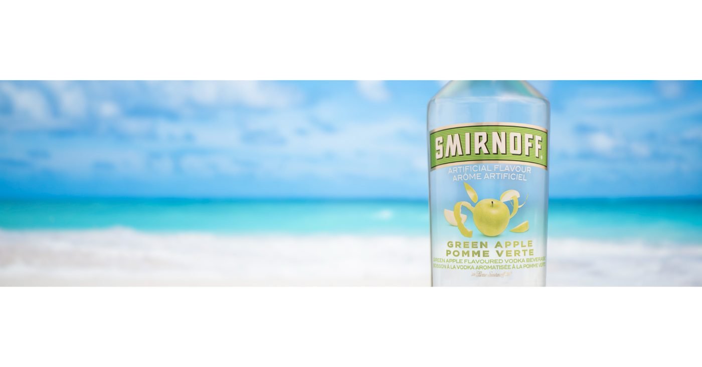 Composited vodka bottle product photography set against a bright tropical beach background