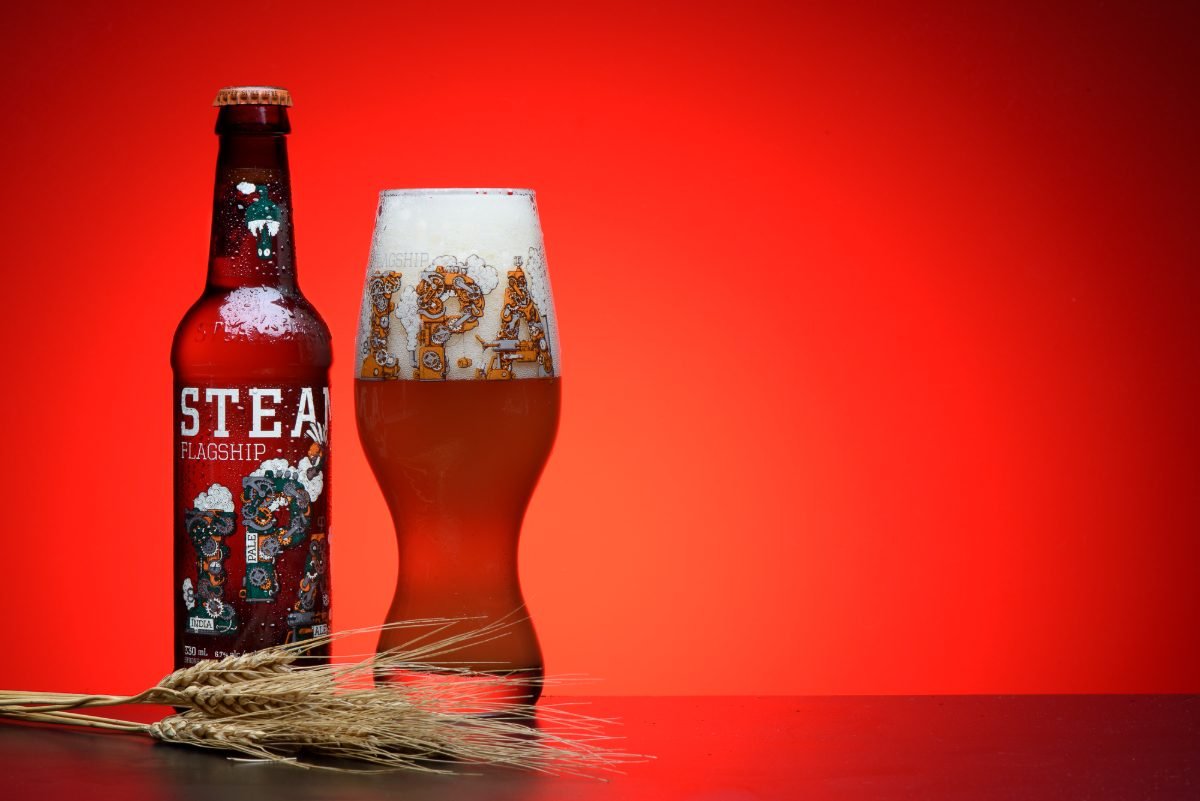 Craft beer product photography of an IPA bottle and branded glass on a saturated red background