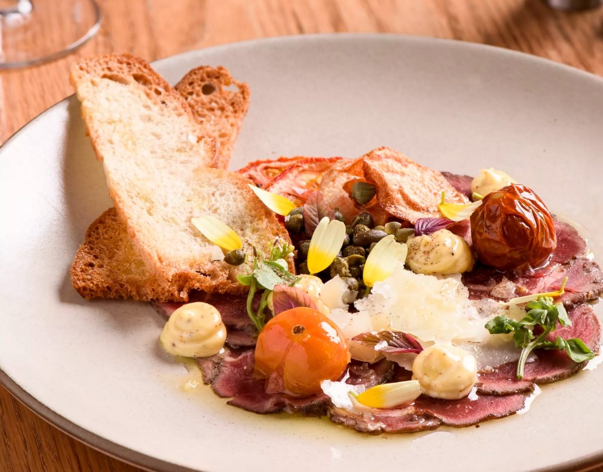 Menu photography of beef carpaccio with capers, parmesan and grilled bread on a ceramic plate