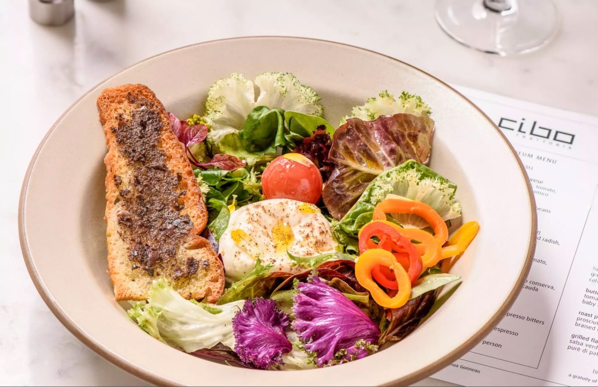 Restaurant food photography of a burrata and garden salad bowl plated beside a menu at a Vancouver trattoria