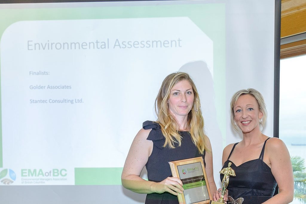 Award winner holding her plaque and trophy in front of the EMA of BC screen at an industry awards night