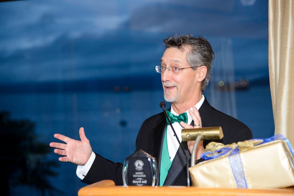 Emcee running the awards program from the podium as the light drops over the water
