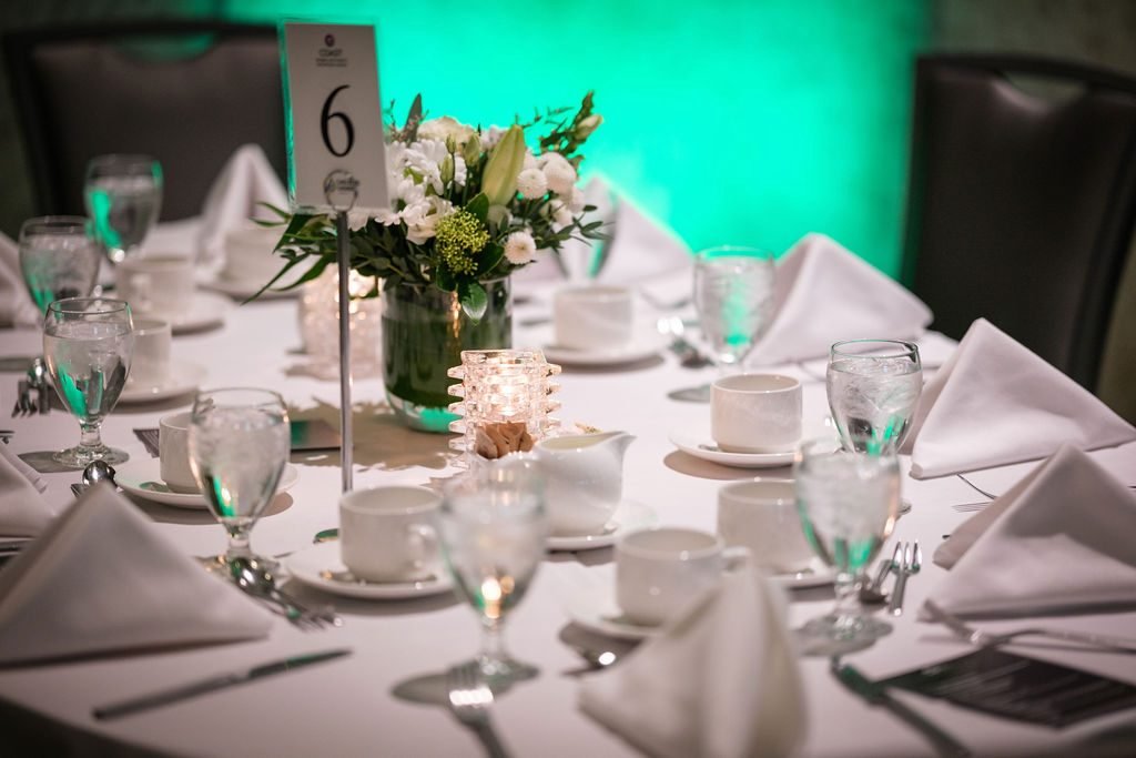 Banquet table setting with floral centrepiece and glassware under coloured lighting at a gala dinner