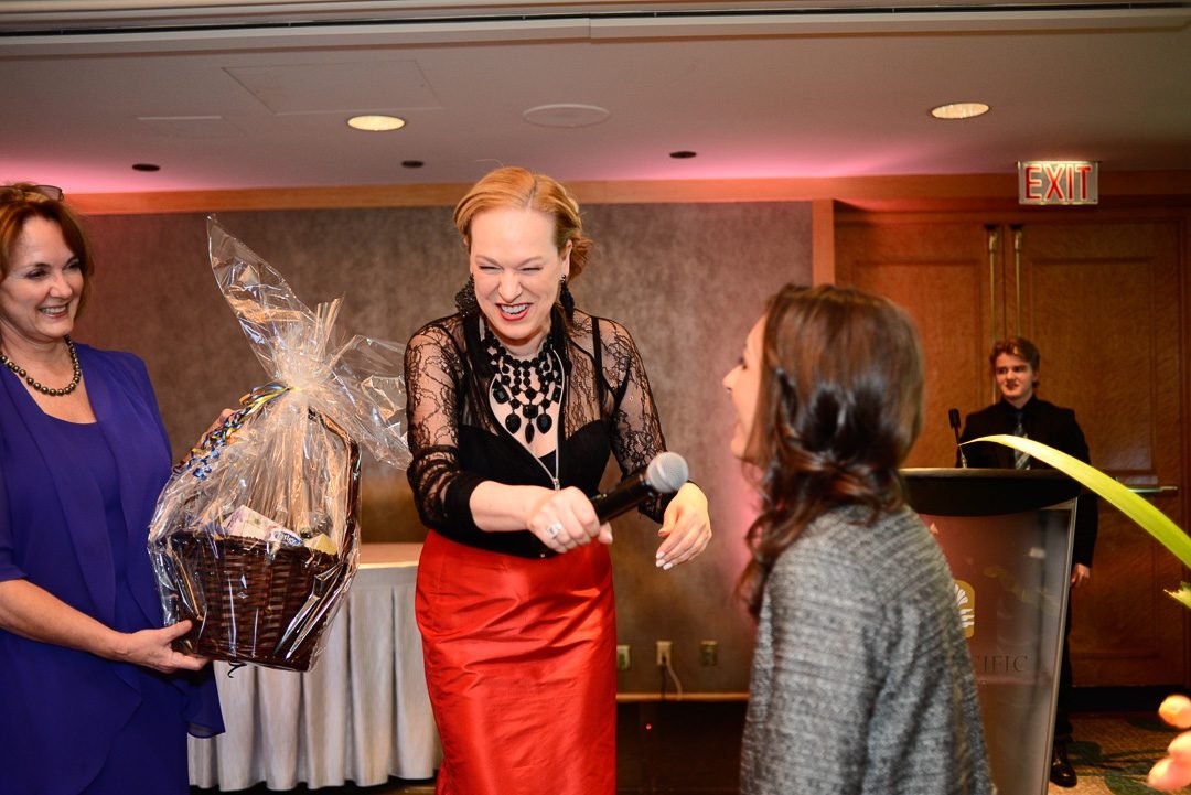 Host presenting a raffle prize basket to a winning guest during a charity gala