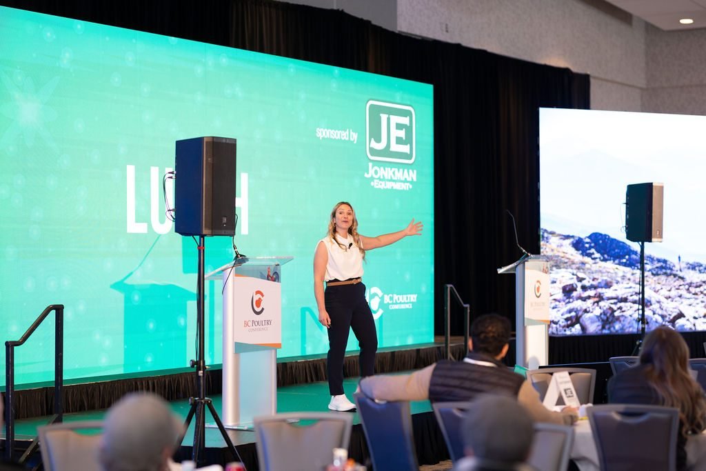 Presenter on stage in front of a sponsor screen at a Lower Mainland corporate conference