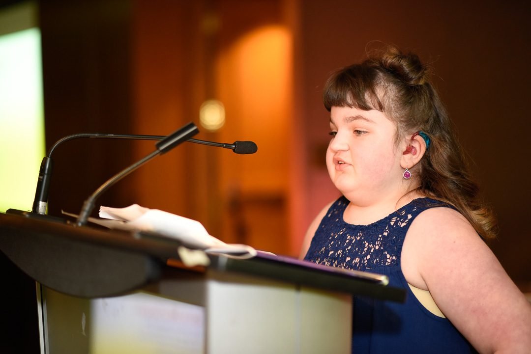 Young guest speaker sharing her story from the podium at a charity fundraising gala