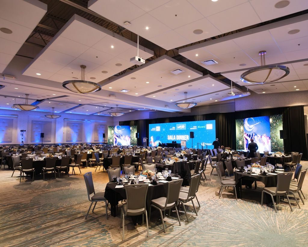 Hotel ballroom set for a corporate gala dinner with stage screens and round banquet tables