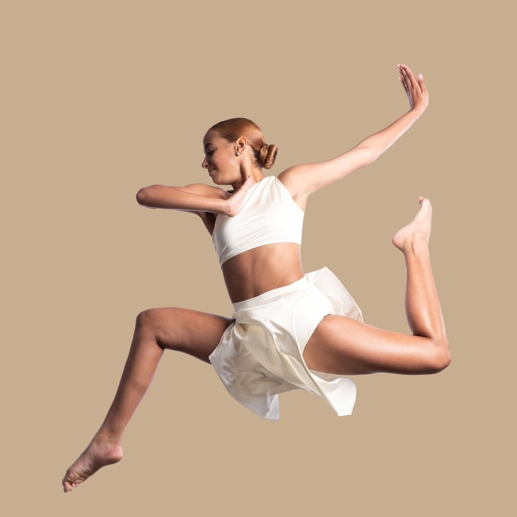 Dancer in a lyrical costume photographed mid-jump on a studio backdrop