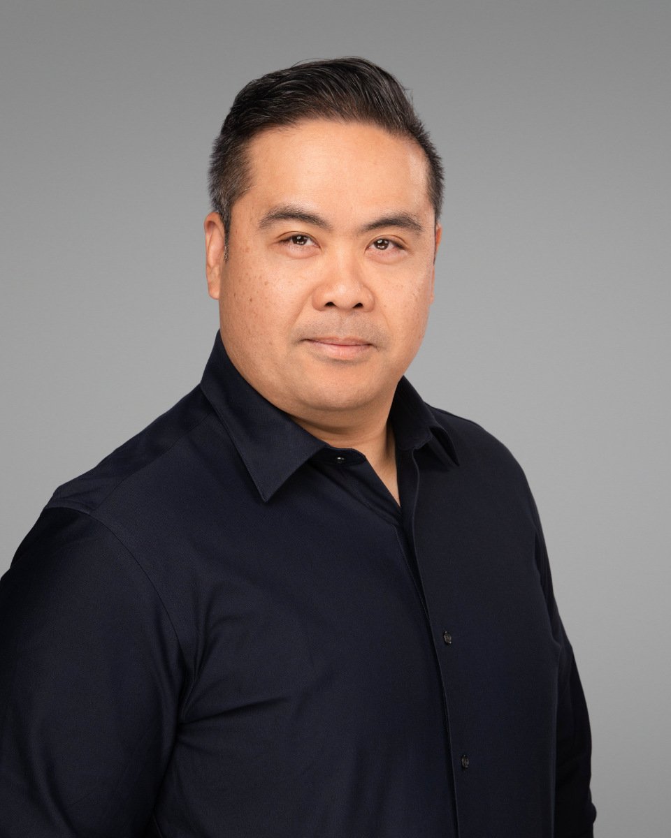 Conference headshot of a man in a black shirt on a grey studio backdrop