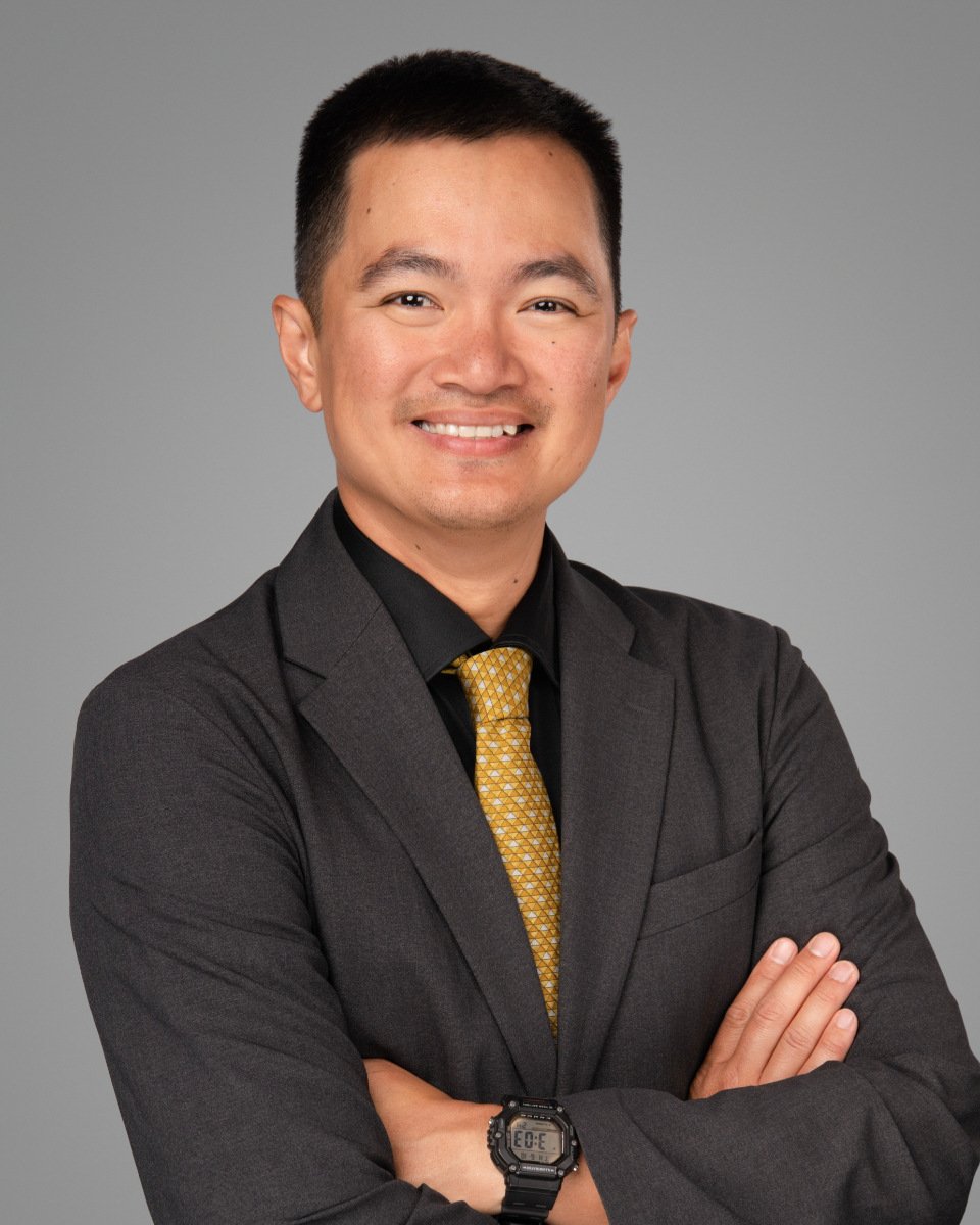 Conference headshot of a man in a charcoal suit and gold patterned tie