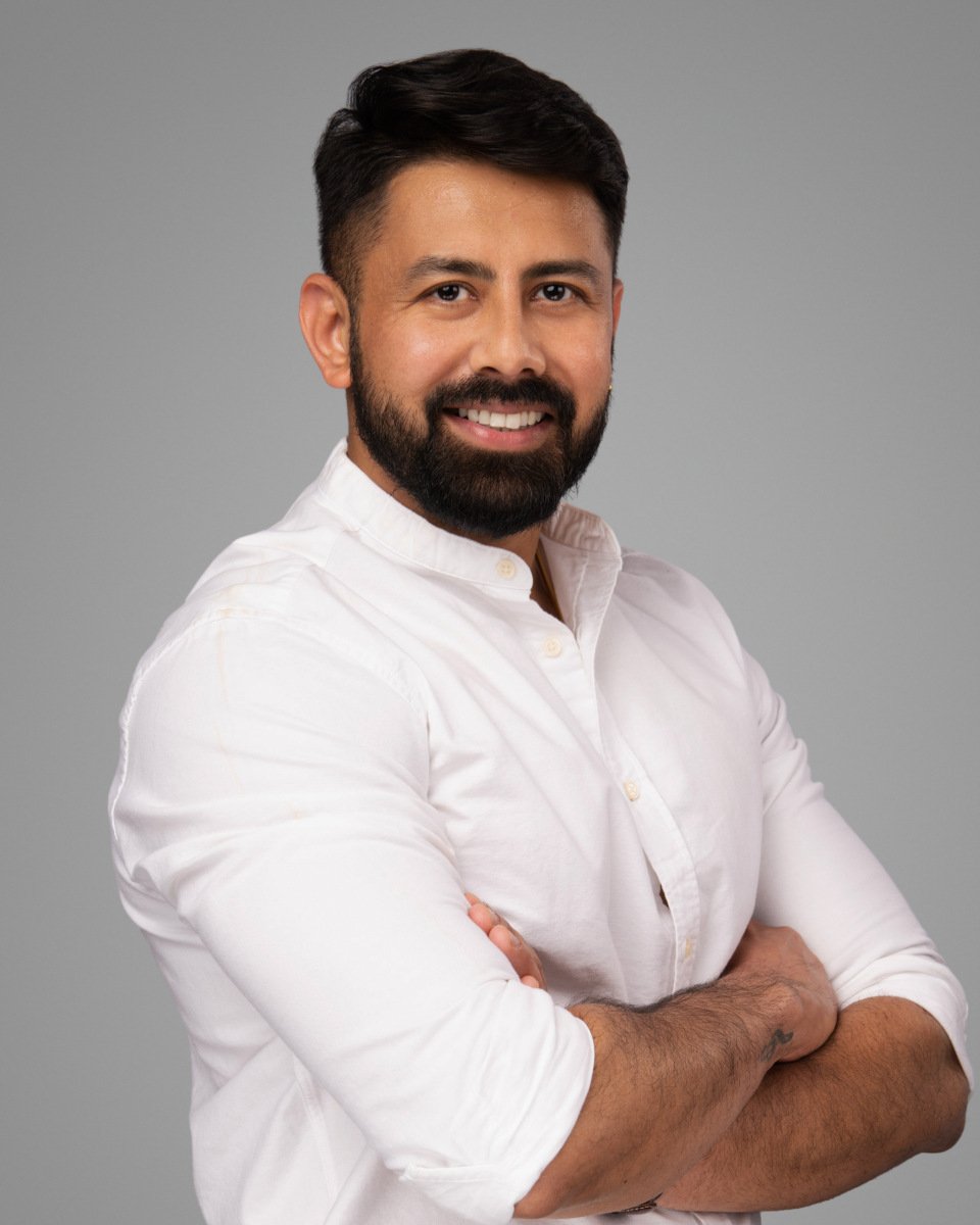 Conference headshot of a bearded man in a white shirt, arms crossed