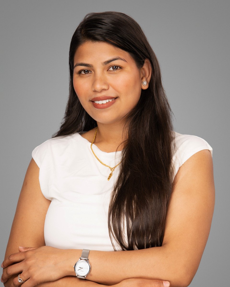 Conference headshot of a woman in a white top with a gold necklace on a grey backdrop