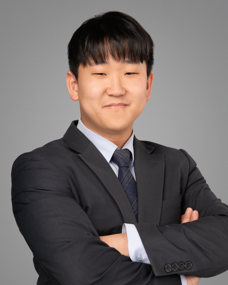 Conference headshot of a young man in a dark suit and tie, arms crossed
